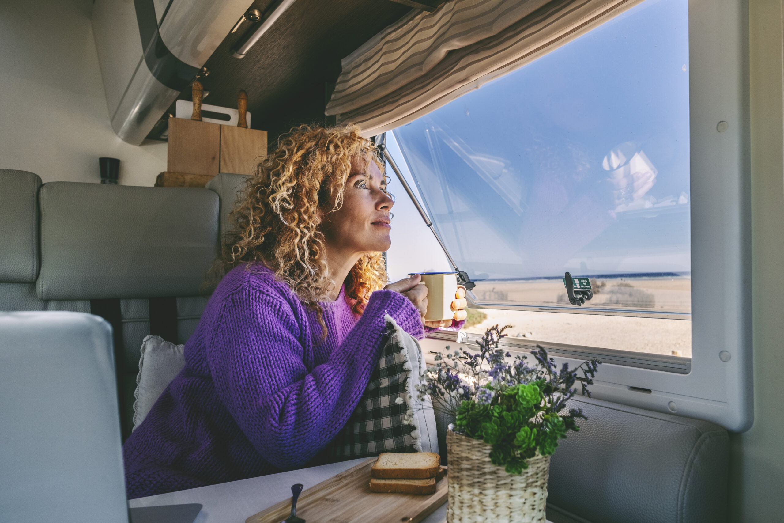 Serene adult woman admiring nature beach sitting inside a modern Serene adult woman admiring nature beach sitting inside a modern camper van in travel holiday vacation. Pretty young female people in van life enjoy coffee and breakfast morning parked free. Freedom